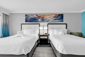 Une chambre d’hôtel avec deux lits, une table de chevet, une œuvre d’art accrochée au mur et un fauteuil vert.