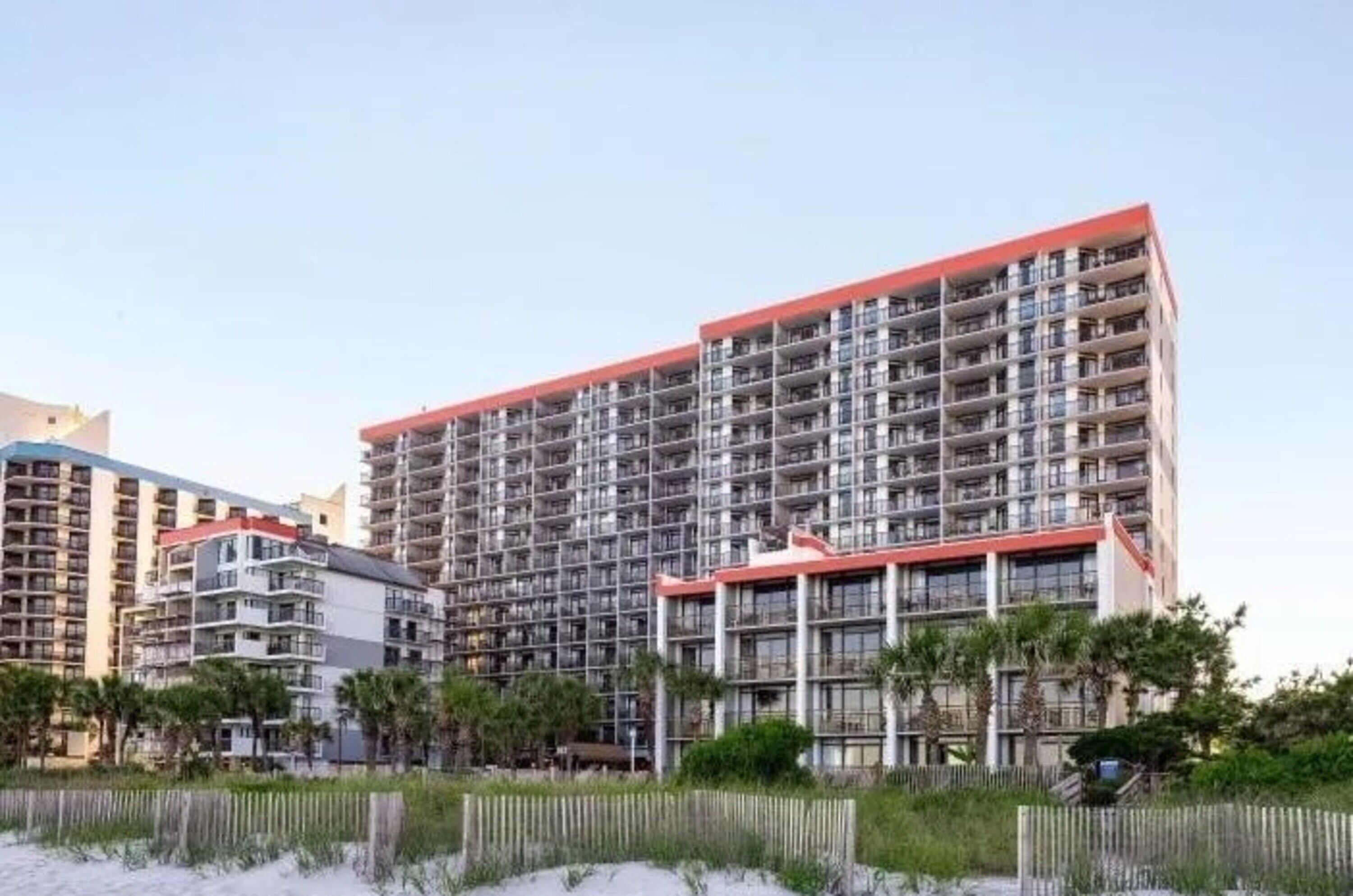 A high-rise hotel with multiple balconies, a red roof, and a beachfront view.