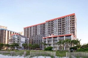 Un hotel de gran altura con varios balcones, techo rojo y vista a la playa.
