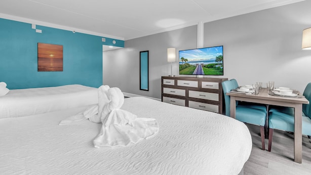 Una camera d'albergo con due letti, una TV, una scrivania con sedie e vista sull'oceano.