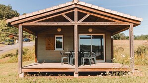 A wooden cabin with a covered porch, two chairs, and a table. - Family Cottage Retreat in Marminiac (Marminiac)