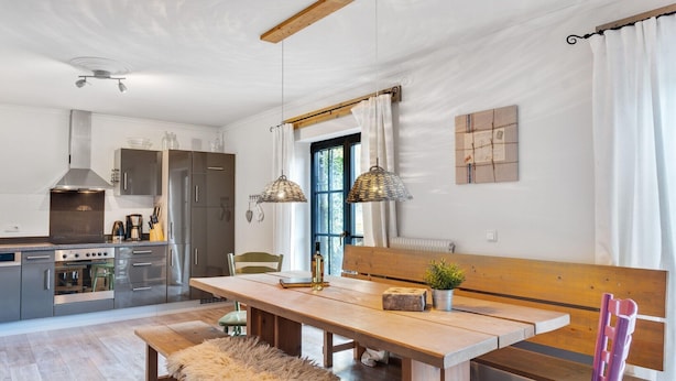 Uma cozinha moderna com mesa de madeira, bancos e luminárias pendentes.