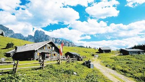 Uma aldeia montanhosa com edifícios de pedra tradicionais, uma bandeira e um caminho de terra.