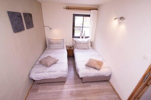 Une petite chambre agréable, dotée de deux lits simples, d’une fenêtre avec des rideaux et d’un plancher en bois.