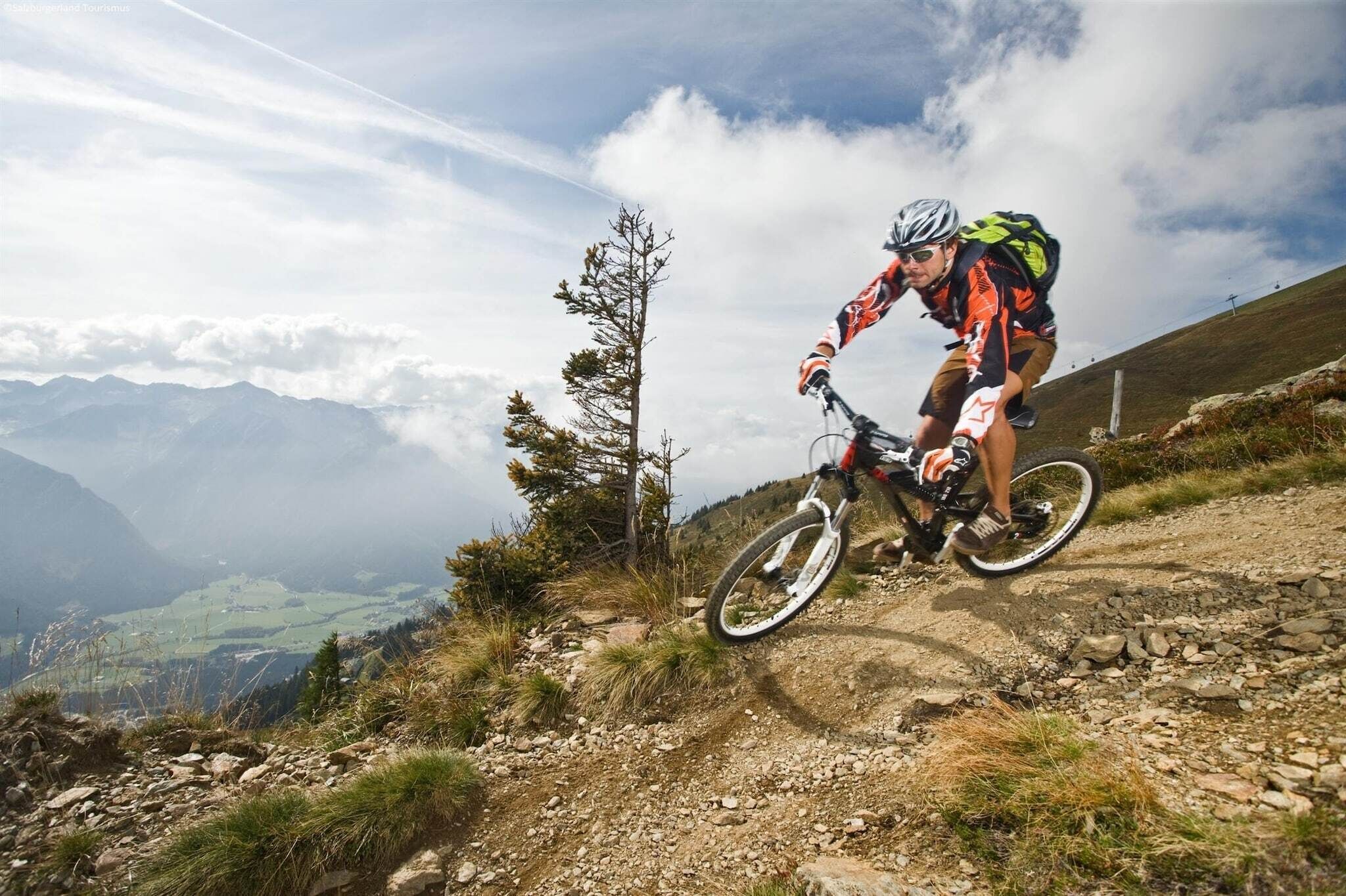 En mountainbiker på en jordvej med udsigt til bjerge og en skyet himmel.