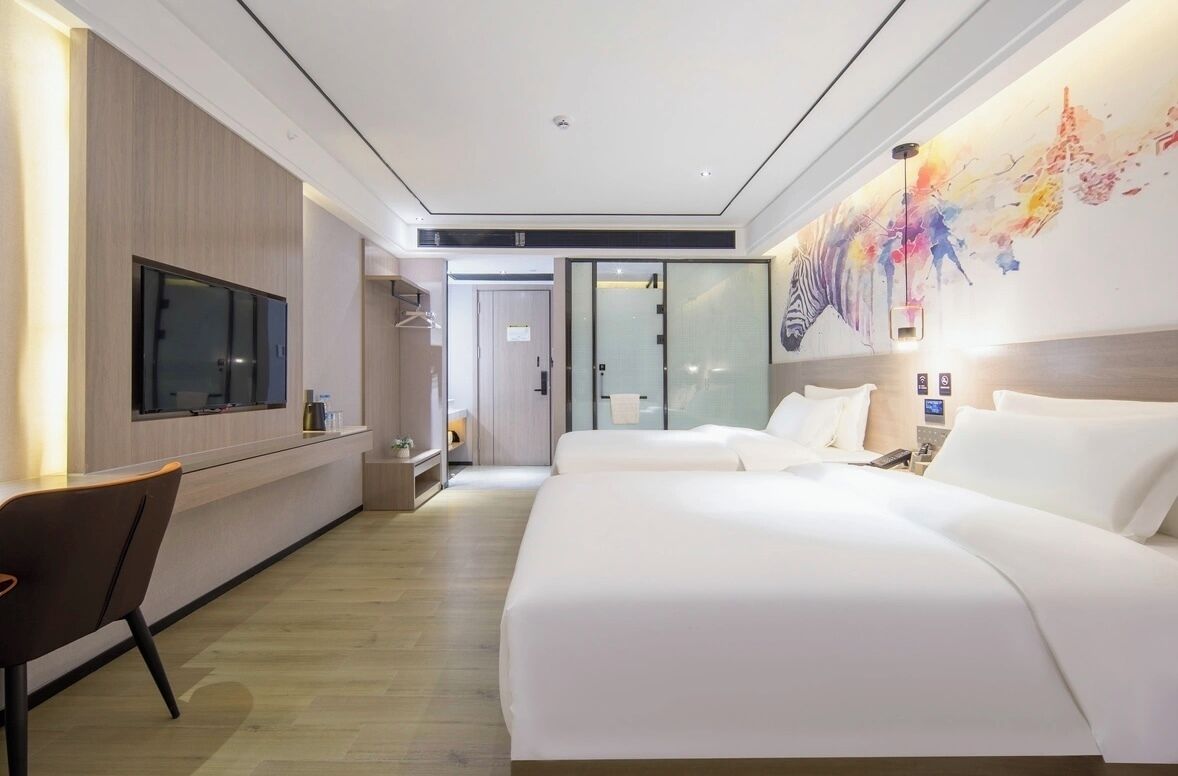 Habitación de hotel con una cama grande, televisión, escritorio y pared divisoria de vidrio.