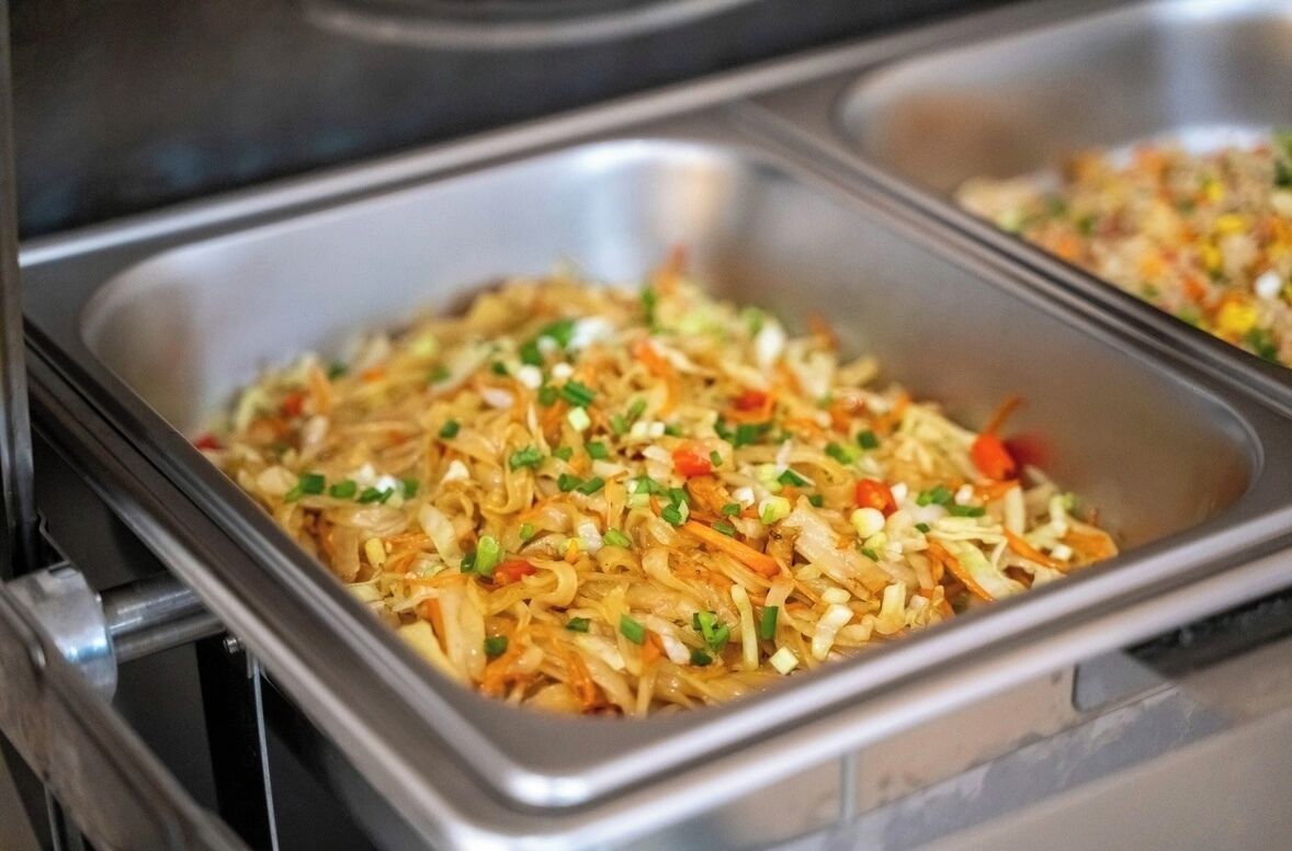 Un bufé con una variedad de platos, entre ellos fideos y verduras.