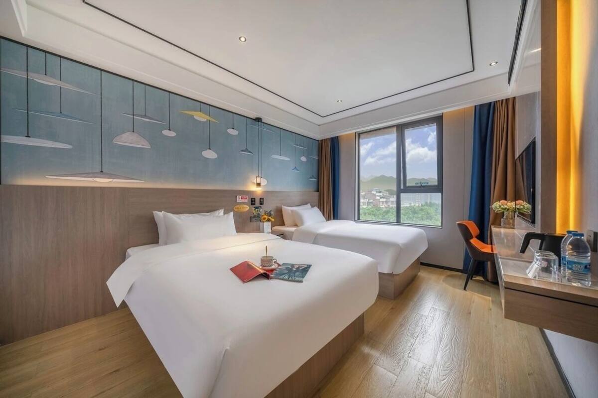 Habitación de hotel con dos camas, un escritorio, una silla, un ventanal con vistas y lámparas colgantes.