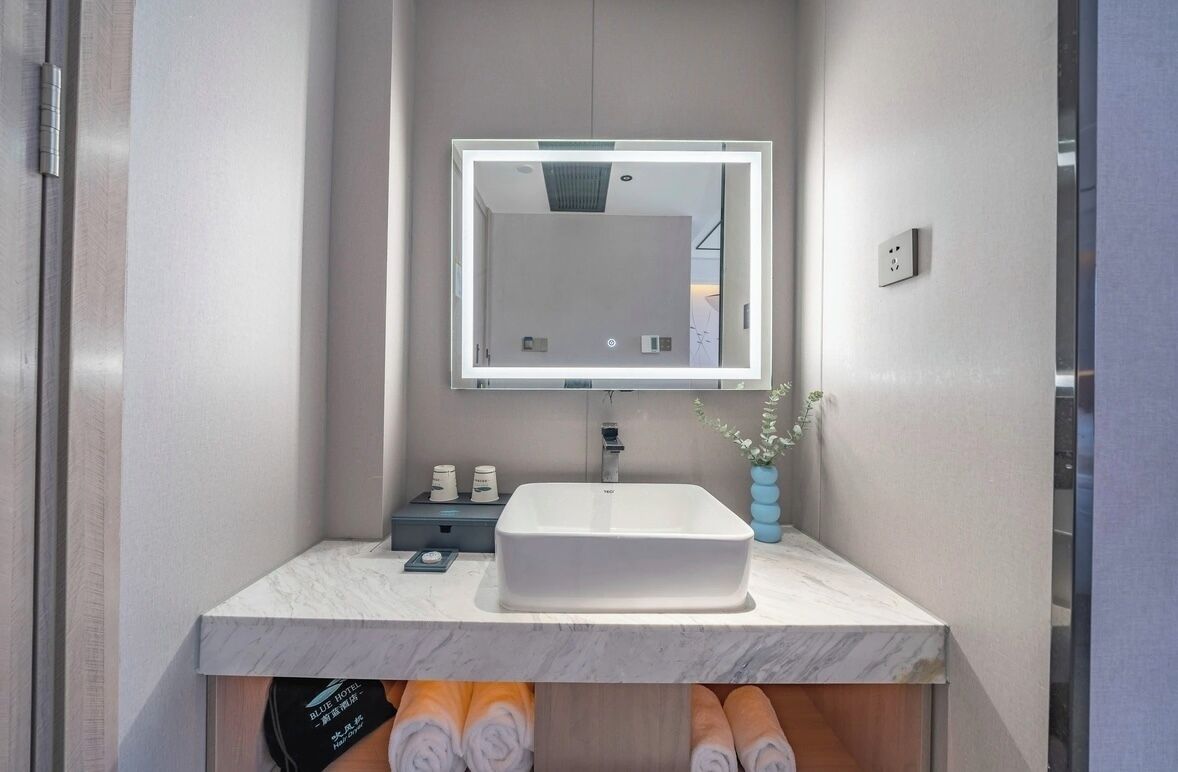 Un baño moderno con un lavabo blanco, un espejo con luz y un florero con flores.