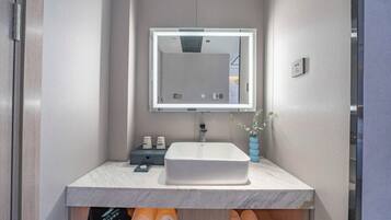 Un baño moderno con un lavabo blanco, un espejo con luz y un florero con flores.