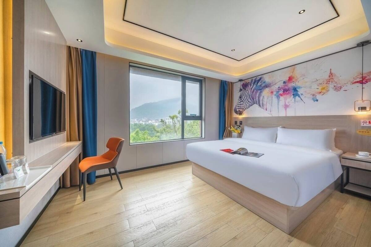 Habitación de hotel con cama, escritorio, silla, televisor y ventana grande con vistas.