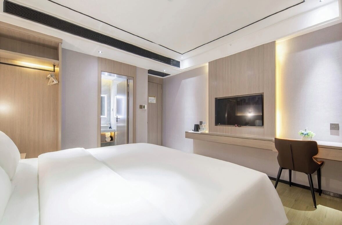 A hotel room with a large bed, a desk with a chair, a television, and a wardrobe.