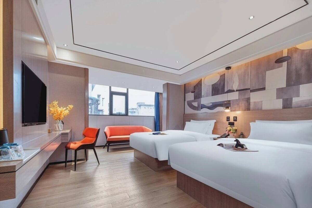 Habitación de hotel con dos camas, un televisor, un escritorio con una silla y ventana con vista a la ciudad.