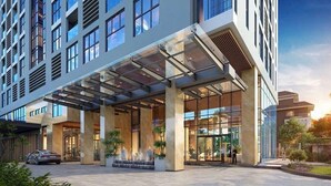En moderne hotelindgang med et overdækket område, store vinduer og et vandelement.