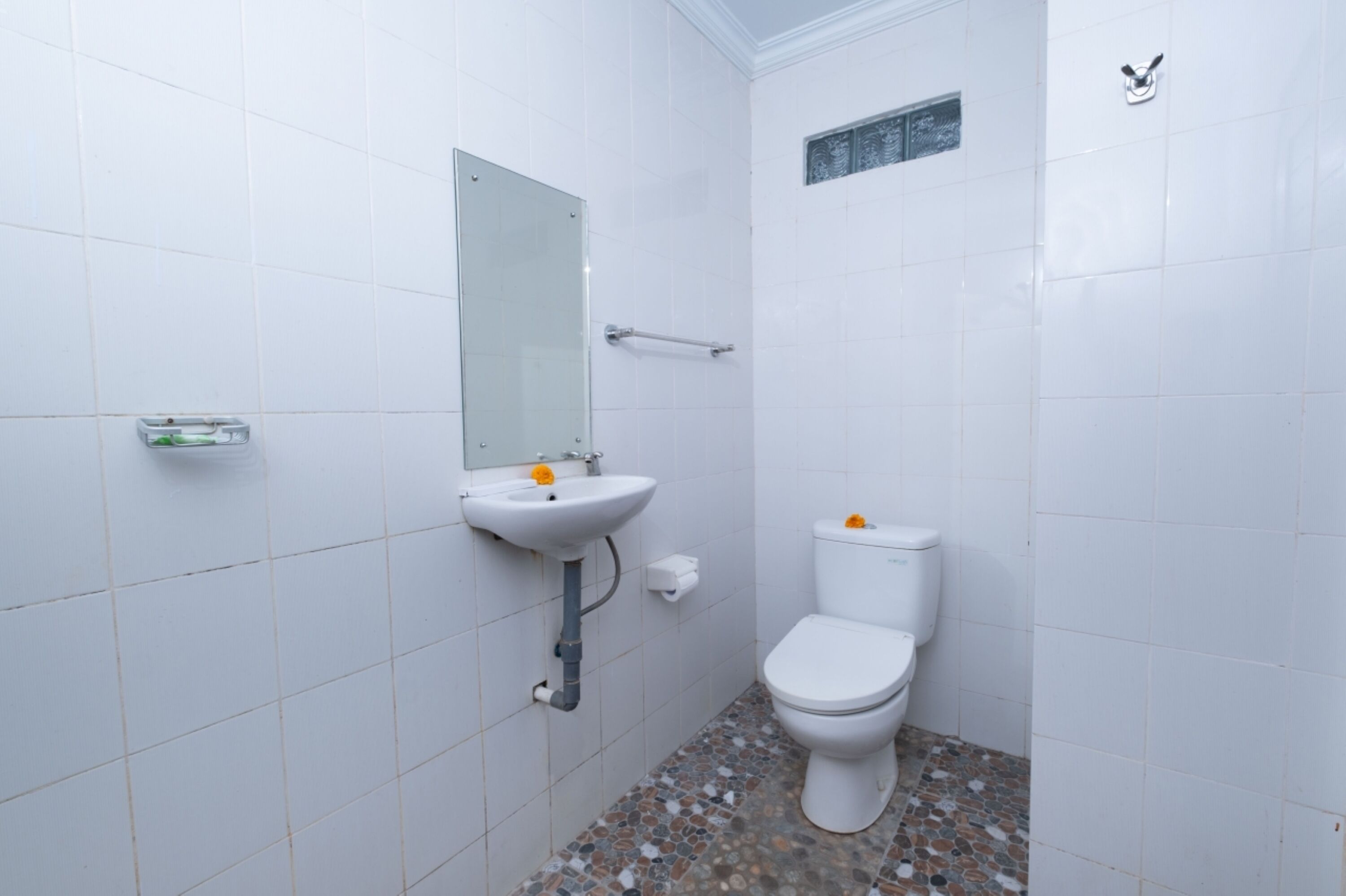 A bathroom with white tiles, a sink, a mirror, a toilet, and a small window.
