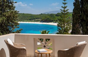 A balcony with wicker chairs, a small table, and a view of a beach and forest. - Bella Mare Hotel (Corfu)