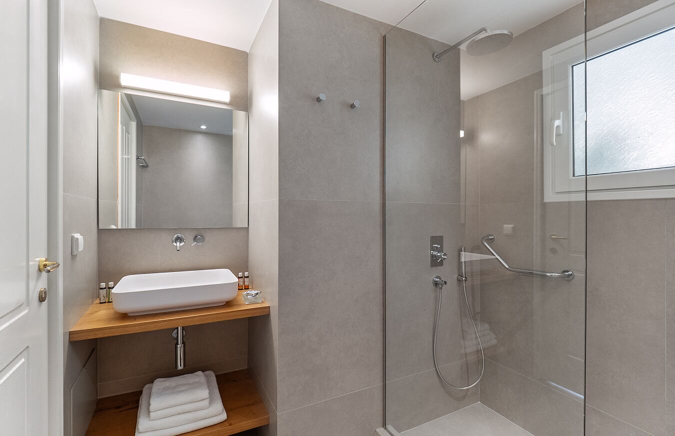 Un baño moderno con ducha envuelta en cristal, tocador de madera y un espejo grande.