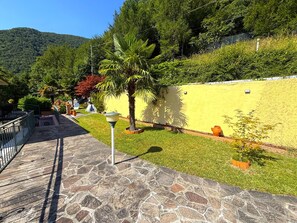 A stone-paved pathway leading to a yellow wall with a palm tree and potted plants. - Apartment House Ammura Balcony Garden (Tignale)