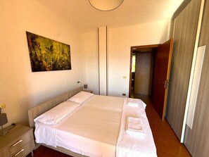 Ein Schlafzimmer mit einem großen Bett, einem Nachttisch, einer Lampe, einem Bild an der Wand und einer Tür zu einem weiteren Raum.