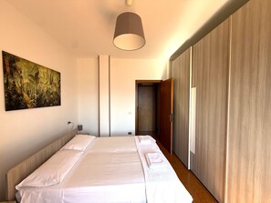 A bedroom with a bed, a painting, a bedside lamp, and a wardrobe. - Ammura Apartment: Balcony, Garden (Tignale)