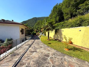 A pathway leading to a building with a stone-paved entrance, surrounded by greenery and a hillside. - Ammura Apartment: Balcony, Garden (Tignale)