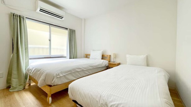 A hotel room with two beds, a window with curtains, an air conditioning unit, and a wooden floor. - LunaStay Apartments - 101 (Sumida-ku)
