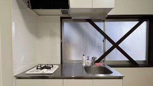A compact kitchen with a gas stove, a small refrigerator, a window with a cross-brace design, and a sink. - LunaStay Apartments - 101 (Sumida-ku)
