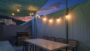 An outdoor patio with a table and chairs, string lights, and a grill.