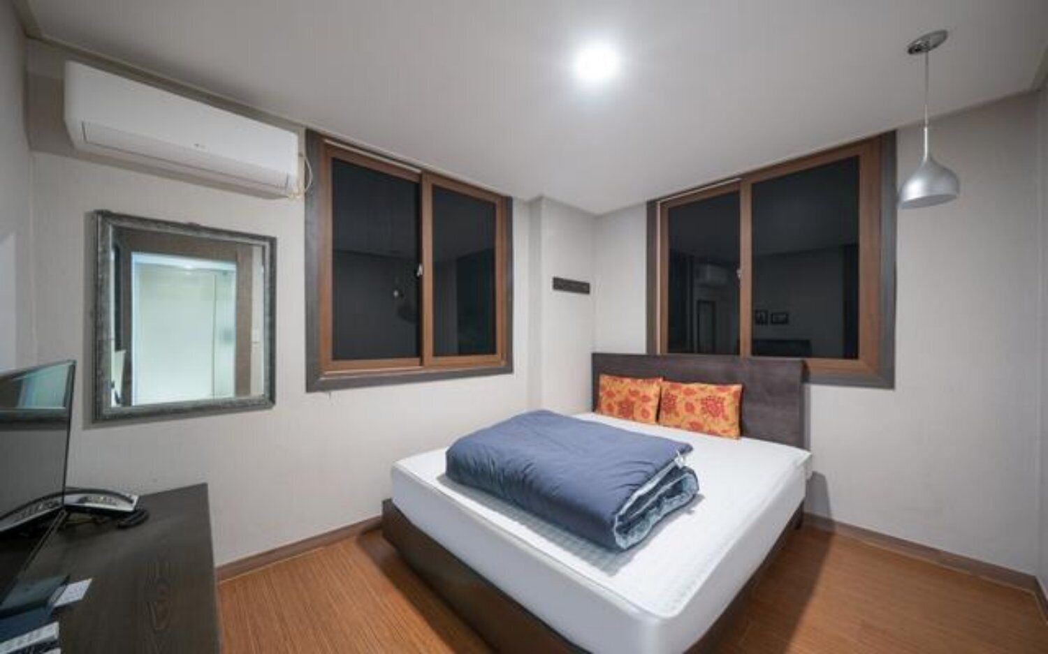 A bedroom with a bed, two windows, a desk, and a hanging light fixture.