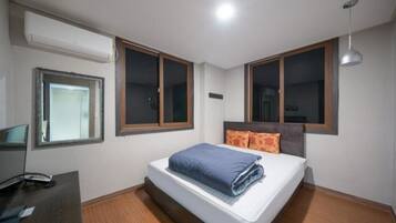 A bedroom with a bed, two windows, a desk, and a hanging light fixture.