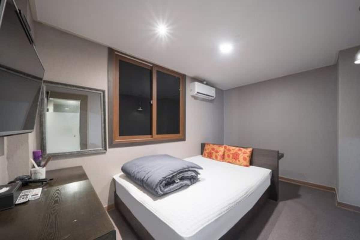 Un dormitorio con cama, escritorio, ventana y aire acondicionado.