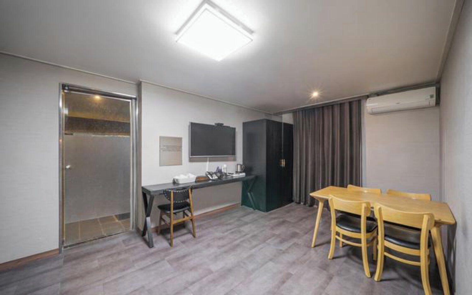 Una habitación con escritorio, sillas, televisor de pantalla plana, puerta y equipo de aire acondicionado.