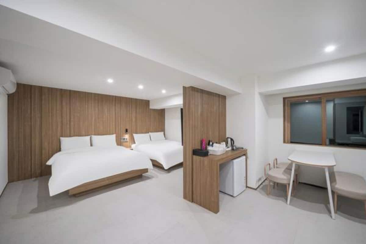 Una habitación de hotel moderna con dos camas, un escritorio, una silla y una kitchenette pequeña.