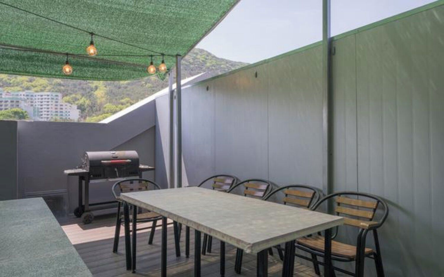 An outdoor patio with a table and chairs, a grill, and a view of the cityscape.