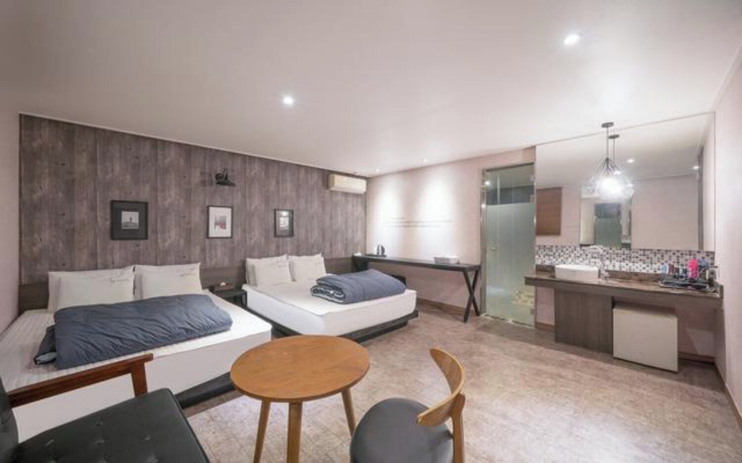 A modern hotel room with two beds, a small dining table, and a kitchenette.
