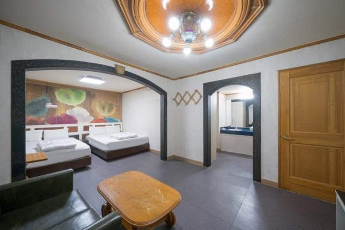 Habitación de hotel con dos camas, una mesita pequeña, un baño con espejo y una puerta de madera.