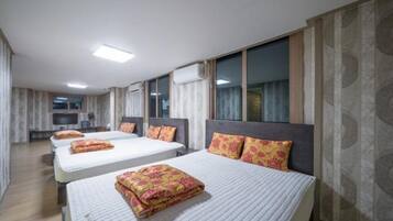 A hotel room with three beds, a flat-screen TV, and a large window.