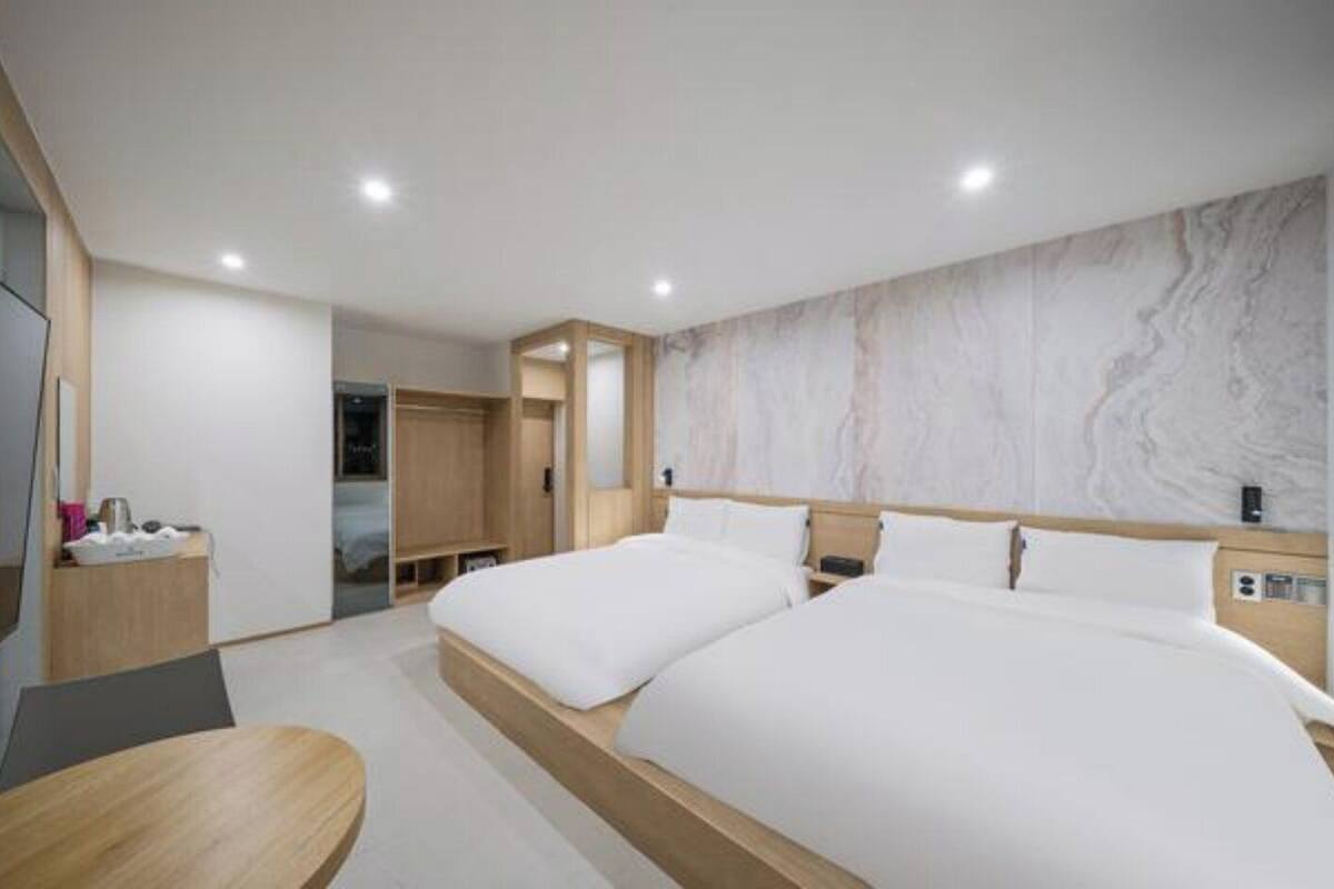 Una habitación de hotel moderna con dos camas, un televisor, un escritorio y un armario.