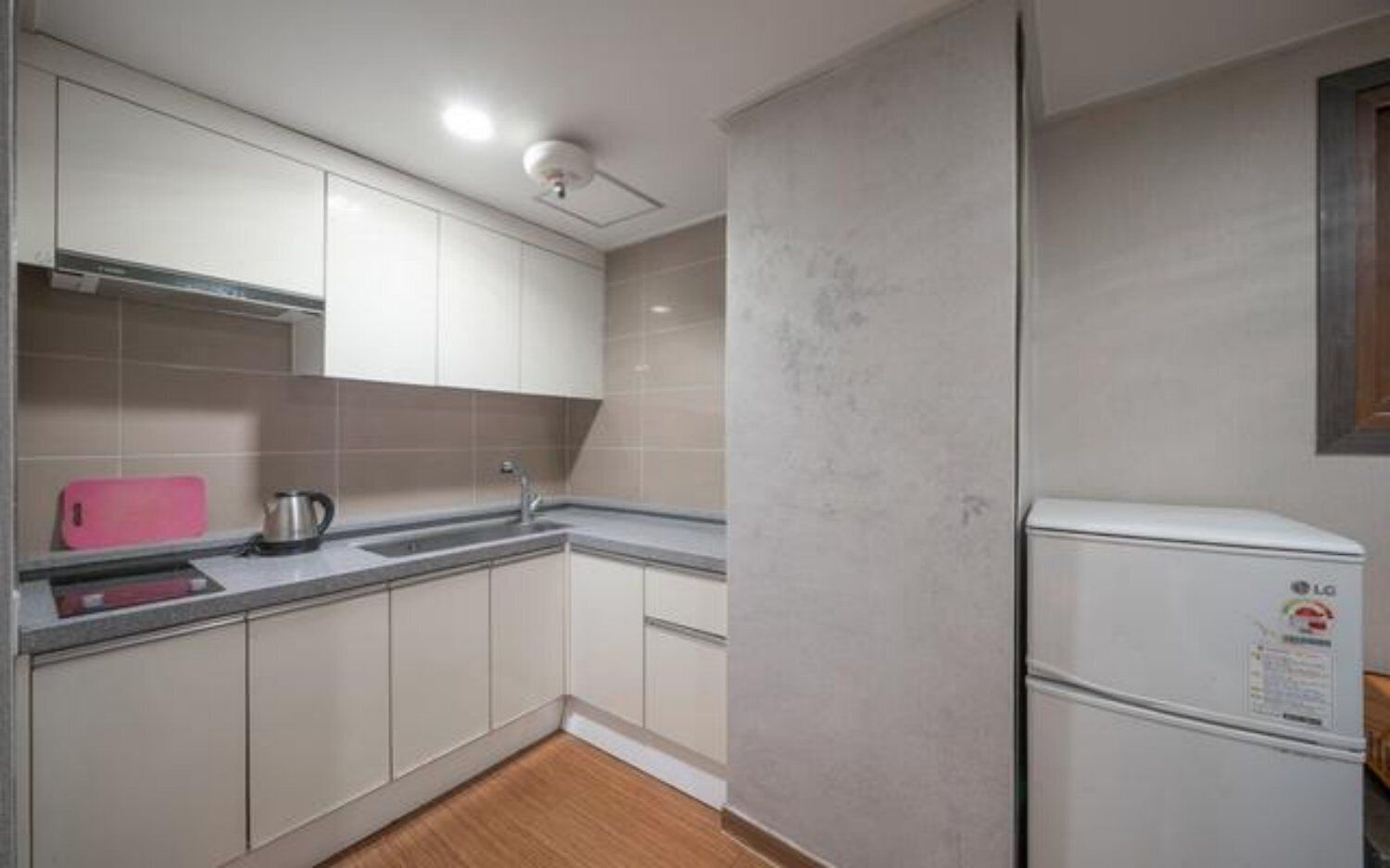 A kitchen with white cabinets, a stainless steel sink, a pink cutting board, a kettle, and a white refrigerator.