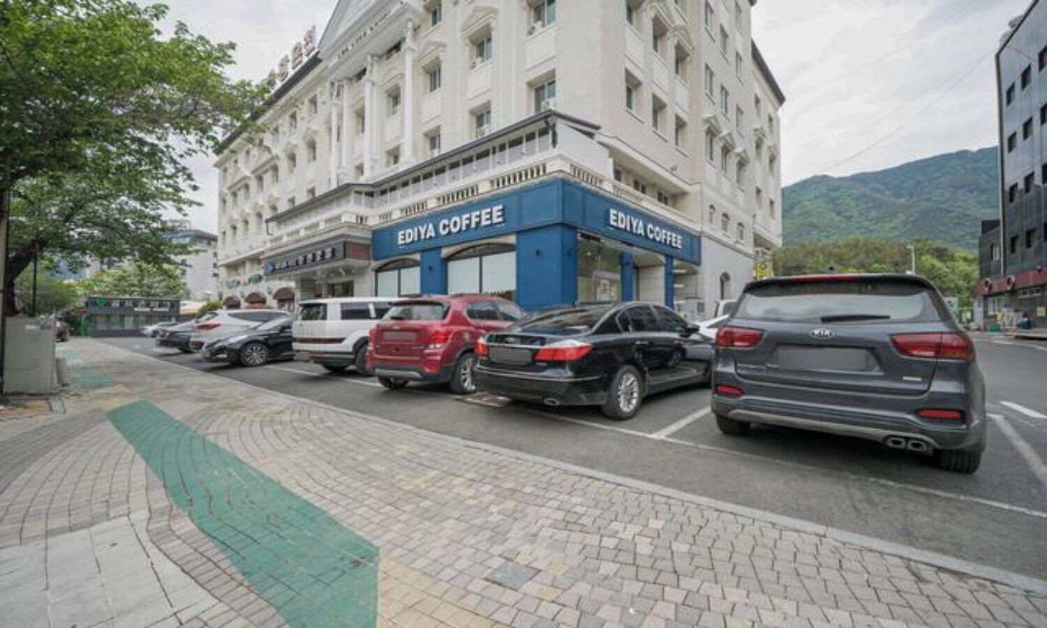 A building with 'EDIYA COFFEE' signage, parked cars, and a paved sidewalk.