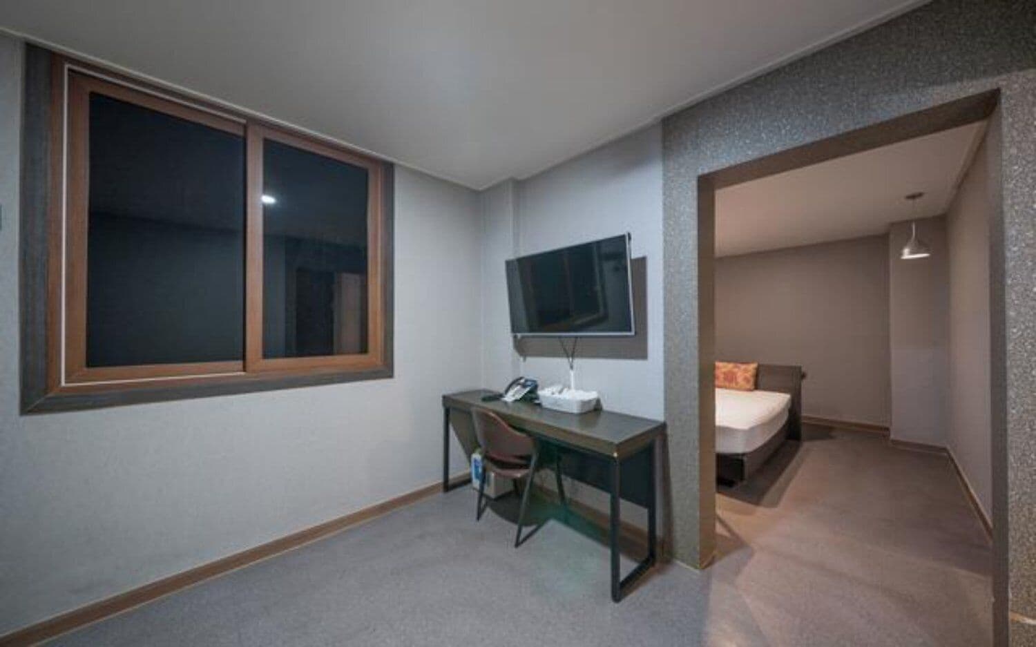 A small room with a desk, chair, bed, and a TV mounted on the wall.