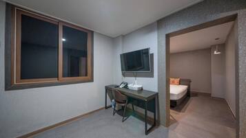 A small room with a desk, chair, bed, and a TV mounted on the wall.
