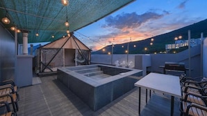 A rooftop terrace with a hot tub, outdoor seating, and string lights.