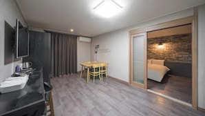 A modern room with a dining area, a kitchenette, and a bed with a brick wall.