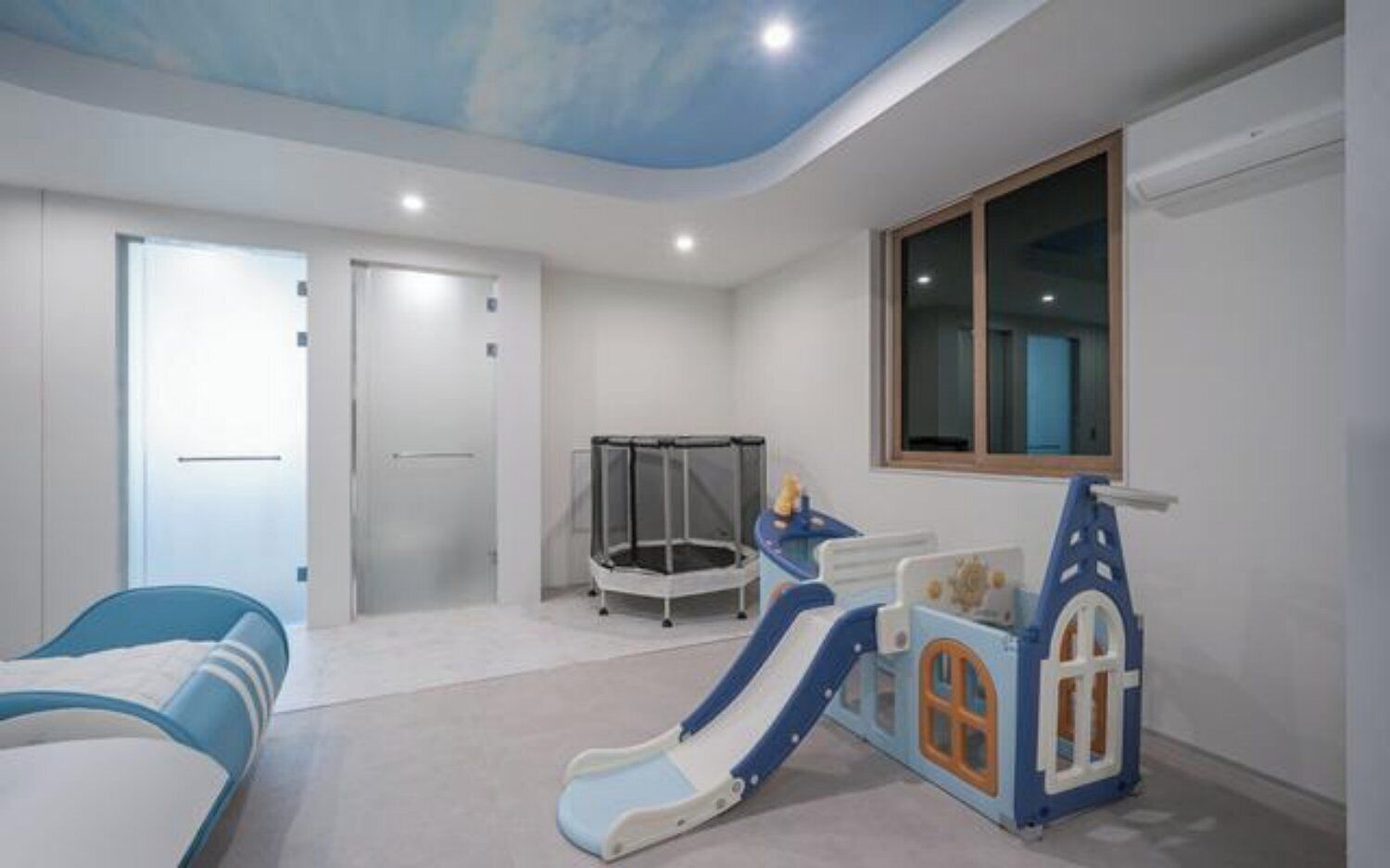 A bedroom with a bed, a play area with a slide, a trampoline, and a window.
