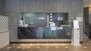 A reception desk with a marble top, a clock, a plant, and a ticket machine.