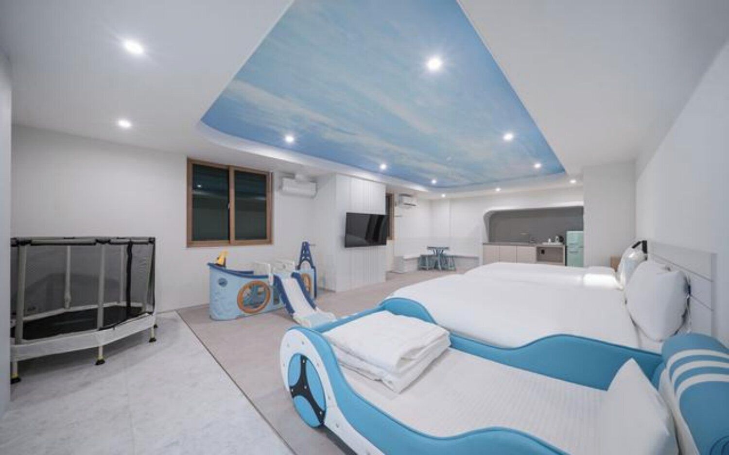 A modern hotel room with a bunk bed, a playpen, a desk, and a kitchenette.