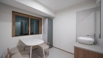 A modern bathroom with a large window, a white sink, and a small table with chairs.