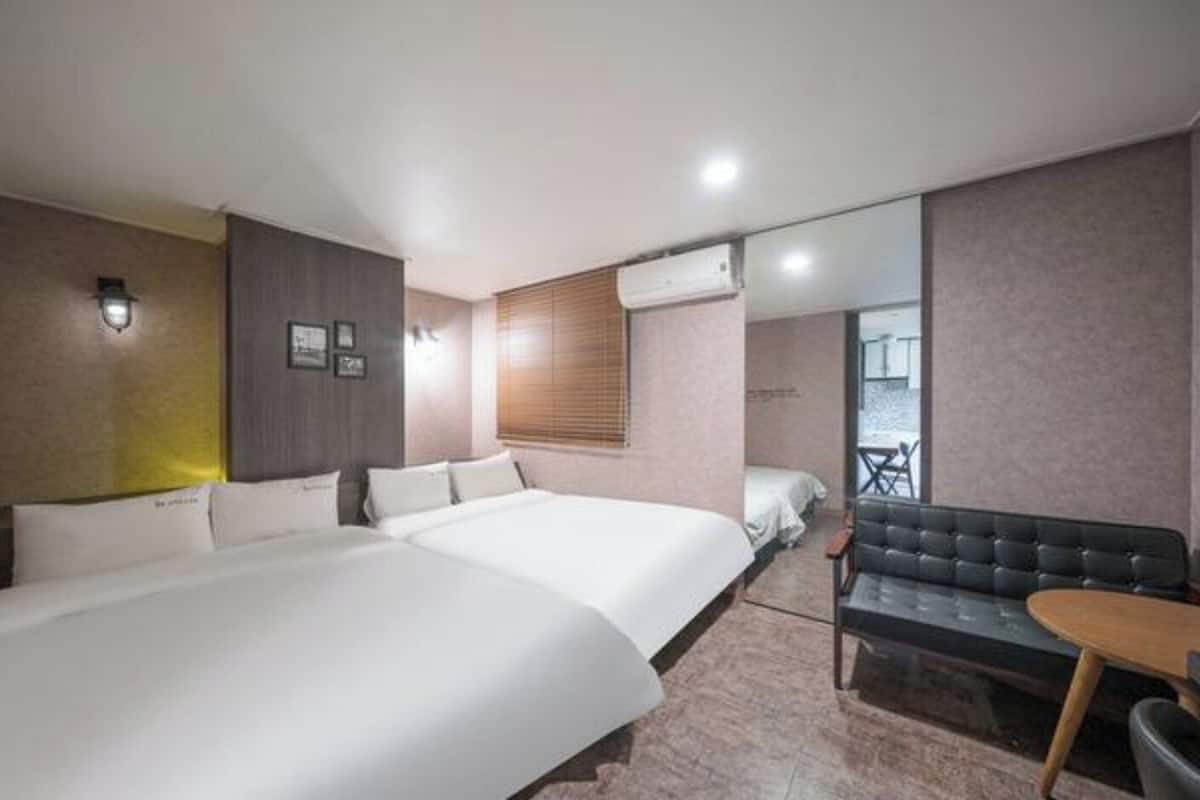 Una habitación de hotel con dos camas, un sofá, una mesa de comedor y un espejo grande.