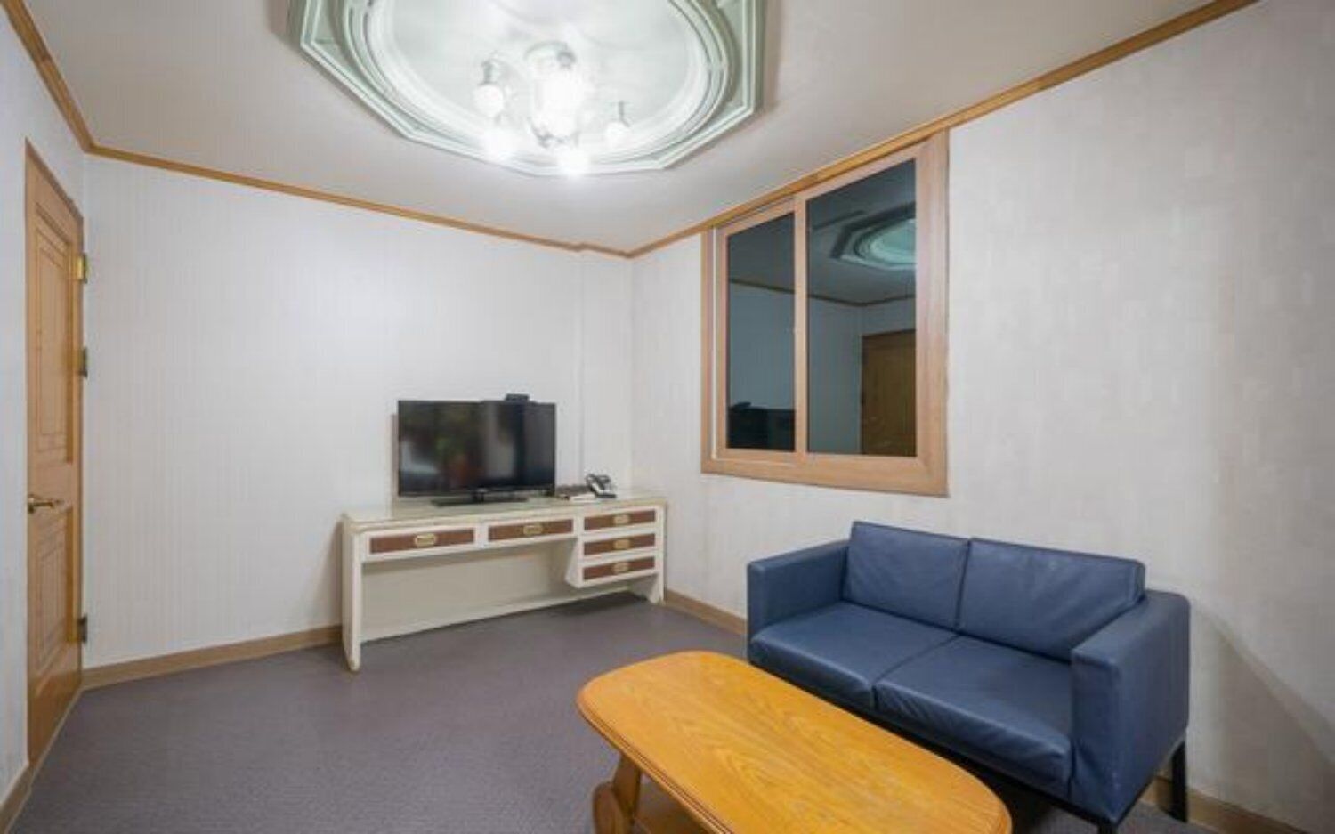 A room with a television on a white cabinet, a blue sofa, and a wooden bench.